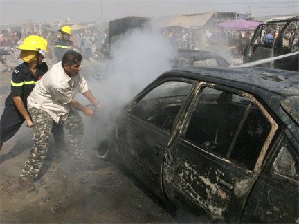 A resident and a fireman try to open the bonnet of a burning vehicle at the site of a bomb attack in Baghdad's Husseiniya district.(Photo: Reuters)