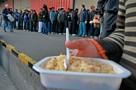 An asylum seeker leaves with rice as others queue,during evening food distribution near the harbour of Calais( Photo: Reuters )