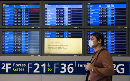 A passenger wears a protective mask as he passes screens with information about H1N1 at Charles de Gaulle Airport north of Paris April 29, 2009(Photo : Gonzalo Fuentes/Reuters)