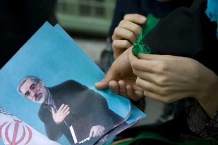 A woman ties a green symbolic ribbon for her friend as she holds a picture of Iran's Presidential candidate Mirhossein Mousavi, during a rally in front of the Tehran Governor's office(Photo: Reuters)