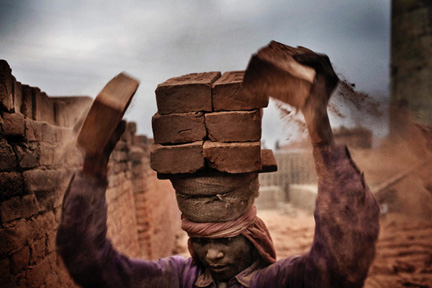 A young worker prepares to carry 12 bricks on his / her head. Carrying the bricks produces a lot of dust that damages the workers’ health.(Credit: Luca Catalano-Gonzaga)