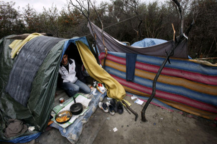 An Afghan migrant cooks in his makeshift shelter in woods near the port of Calais on 23 September, 2009(Photo: Reuters)