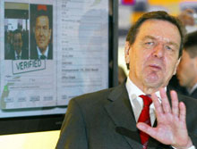 Le chancelier allemand Gerhard Schröder&nbsp;pose devant une reproduction de son passeport biométrique. 

		(Photo : AFP)