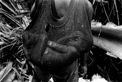 <strong>Les Kopkaka (Papous), Irian Jaya, <br />Indonésie, 1997<br /></strong>Dans la jungle marécageuse, un enfant Kopkaka dort dans un filet fait de fibre végétale, pendant que son père extrait de la moelle de sagoutier, principal aliment des ethnies vivant dans les basses terres marécageuses.© Musée de l'Homme