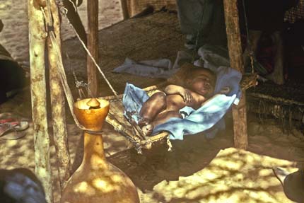 Le bébé dort dans un berceau-hamac, suspendu aux piquets de la tente. Ainsi, on peut doucement le balancer. Le berceau est fait d'écorce de tamat (Acacia ehrenbergiana) et de paille d'afazo (Panicum turgidum). Au premier plan, on remarque une calebasse en forme de gourde que les petites filles utilisent pour baratter le lait. 1982 &#13;&#10;&#13;&#10;&#9;&#9; ©IRD/Edmond Bernus
