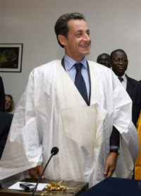 Nicolas Sarkozy a reçu comme cadeau un boubou blanc et or, nettement surdimensionné, qu’il a malgré tout enfilé par-dessus son costume. 

		(Photo : AFP)