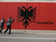 Lundi 11 février 2008. Des Albanais du Kosovo passent devant un gigantesque drapeau où il est inscrit : « Heureuse indépendance »(Photo : Reuters)