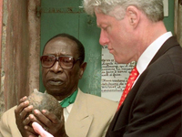Joseph Ndiaye avec le président américain Bill Clinton, en avril 1998. Dans ses mains, une boule de 10kg qui était utilisée pour empêcher les détenus de s'enfuir de Gorée. ( Photo : Paul Richard / AFP )