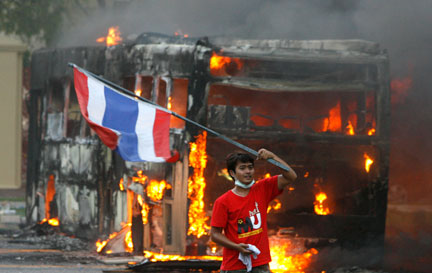 Un partisan de l'ancien Premier ministre en exil Thaksin Shinawatra brandit le drapeau national thaïlandais devant un bus en flamme, lors d'une manifestaion antigouvernementale à Bangkok, le 13 avril 2009.(Photo : Reuters)