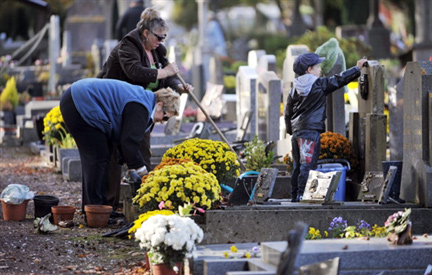Deux femmes et un enfant nettoient une tombe dans un cimetière à Caen.(Photo : AFP)