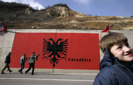 Lundi 11 février 2008. Des Albanais du Kosovo passent devant un gigantesque drapeau où il est inscrit : « Heureuse indépendance »(Photo : Reuters)