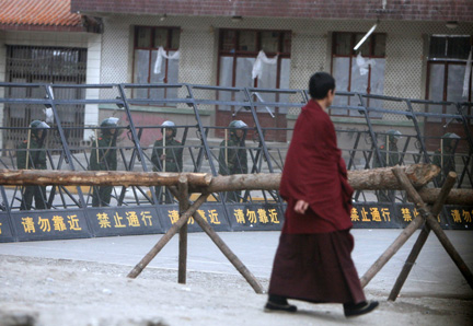 Un moine tibétain passe devant les policiers postés derrière les barricades qui séparent les parties chinoise et tibétaine de la ville de Xiahe (province de Gansu).(Photo : Reuters)